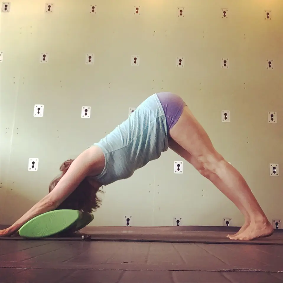 A student holding downward-facing dog with a block under the head at Palm Yoga in Tampa
