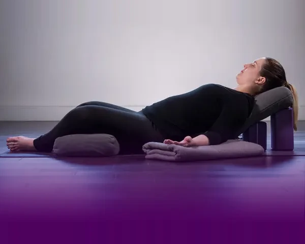 Student resting in a supported restorative yoga pose with bolsters and a block at Palm Yoga in Tampa